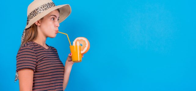 młoda kobieta pije pomarańczowy sok na niebieskim tle